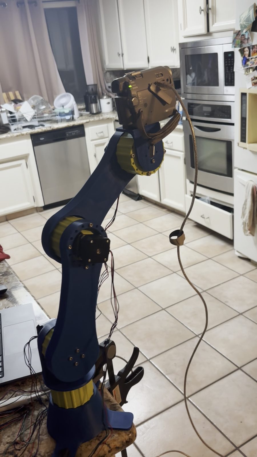 CLARK arm standing upright on a kitchen counter during the five-day build, links in dark blue with yellow gearbox housings, wiring loose.