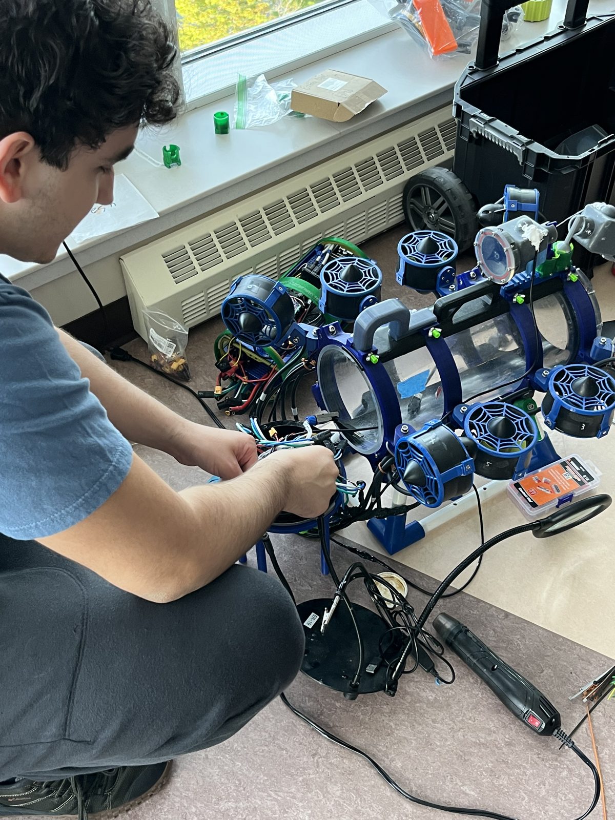 Me seated on the floor working on the ROV's internal electronics with the frame open.