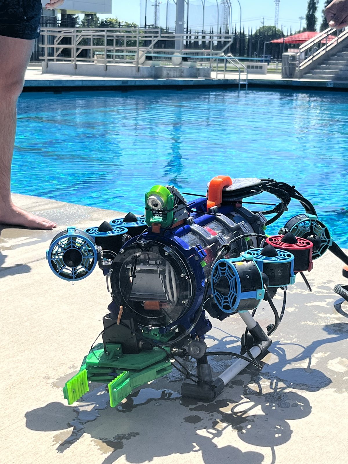 Crush Depth ROV on a pool deck: black frame, blue thruster guards, green manipulator, cameras and cabling visible.
